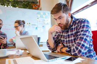 Concentrated Man Reading on Laptop at Desk